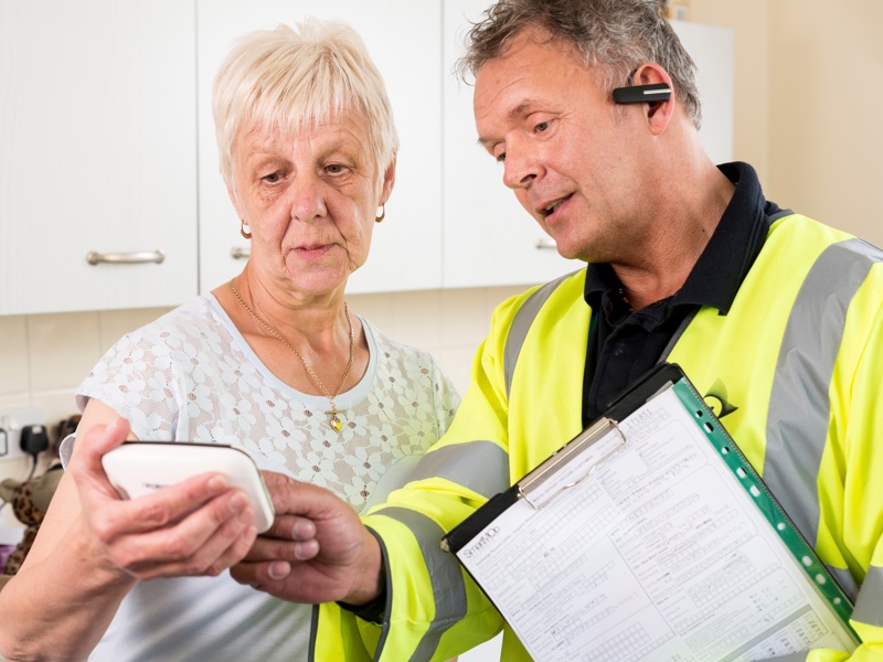 a man in PPE, showing a mature lady how to use a smart meter.