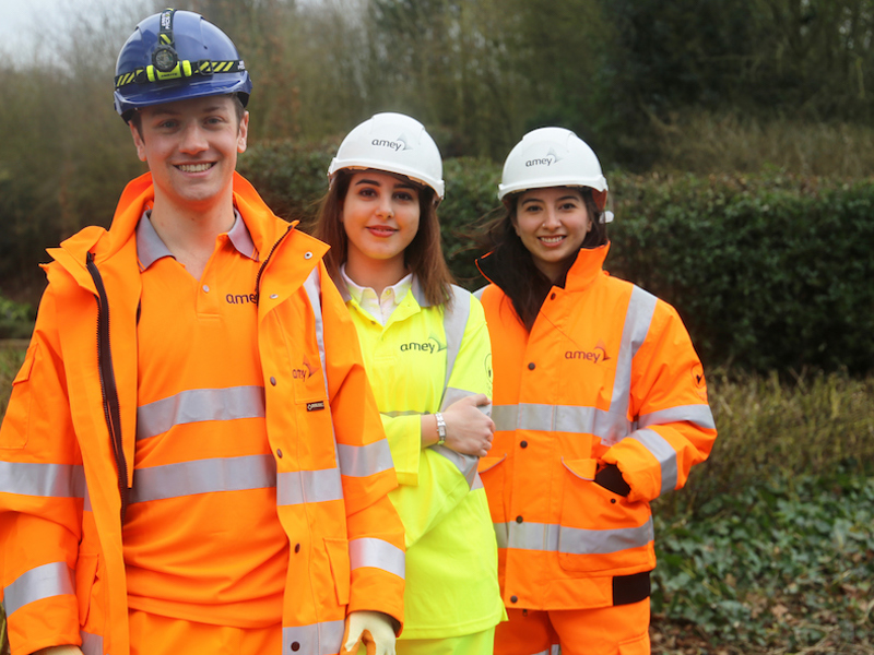 Image of three Amey employees in PPE stood in a field, looking out to the distance.