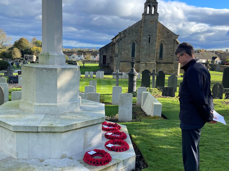 Image of a man standing at a poppy memorial in a cemetery.