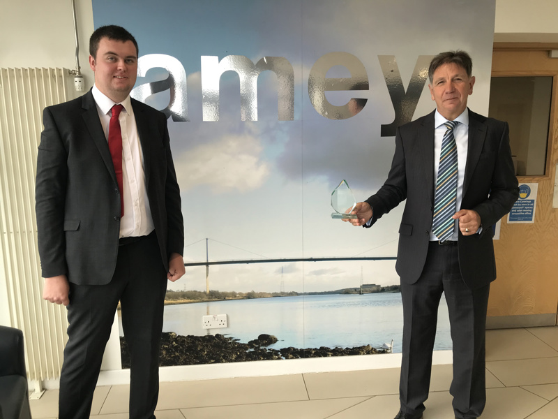 Two men in suits, holding an award.