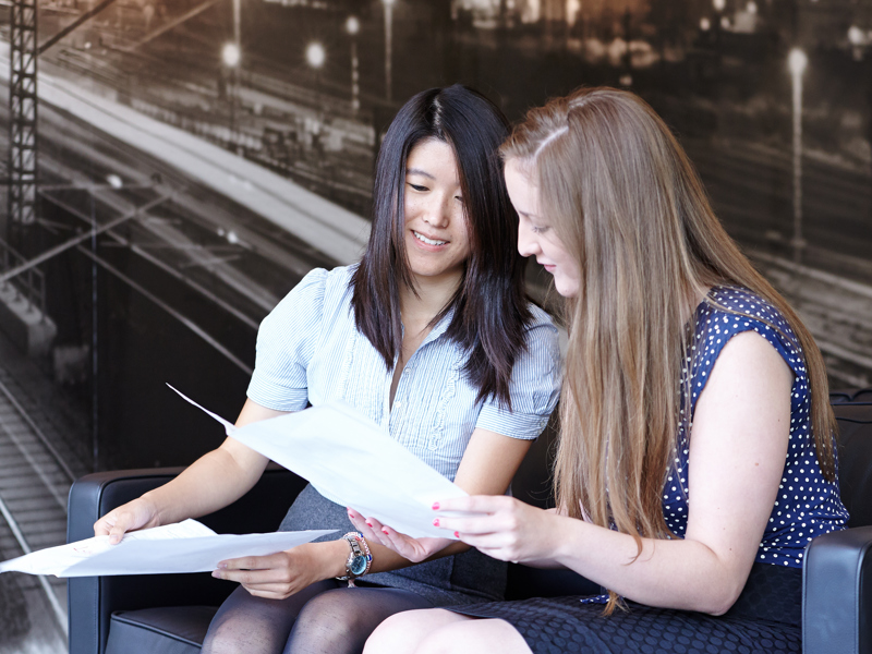 Two females inspecting a document as a coffee table.