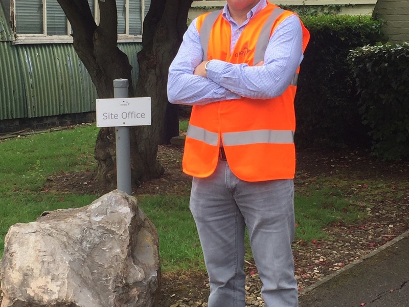Image of an Amey employee, stood on the pavement in front of an Amey office sign.