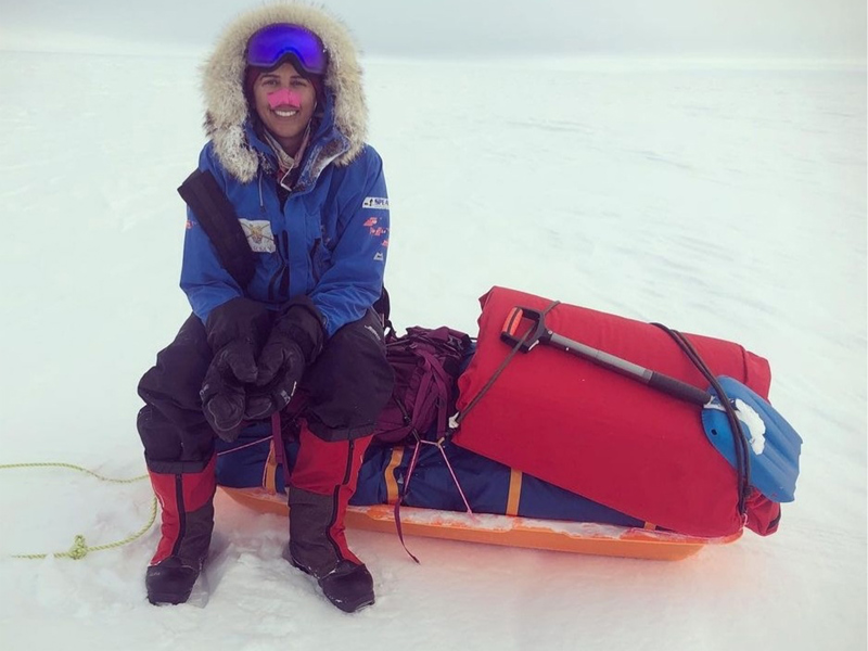 Image of a man in snow gear sat on a sledge in the snow.