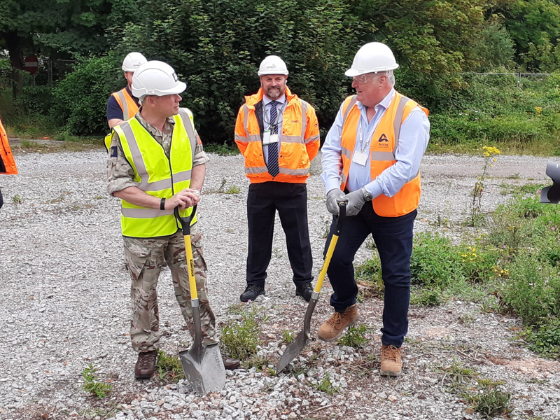 Three men, earing hi vis jackets, holding shovels. 