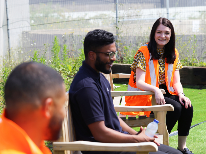 side view image of Amey employees sat on garden benches.