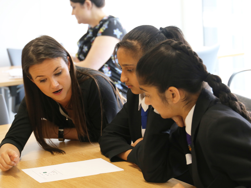 Three woman at a desk, inspecting a document.