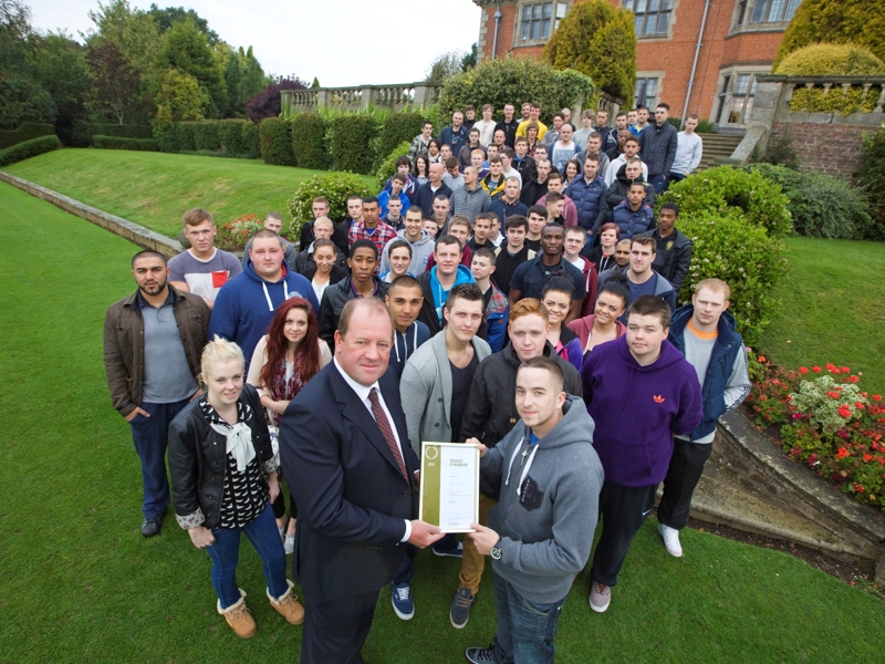 A large gathering of people, holding a certificate. 