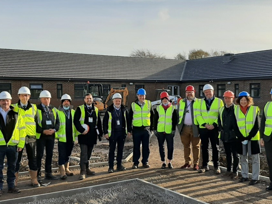 A group of Amey employees stood in a line in PPE in front of a building.