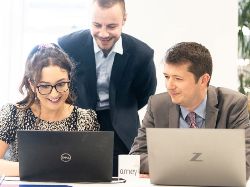 Amey employees collaborating in front of two laptops.