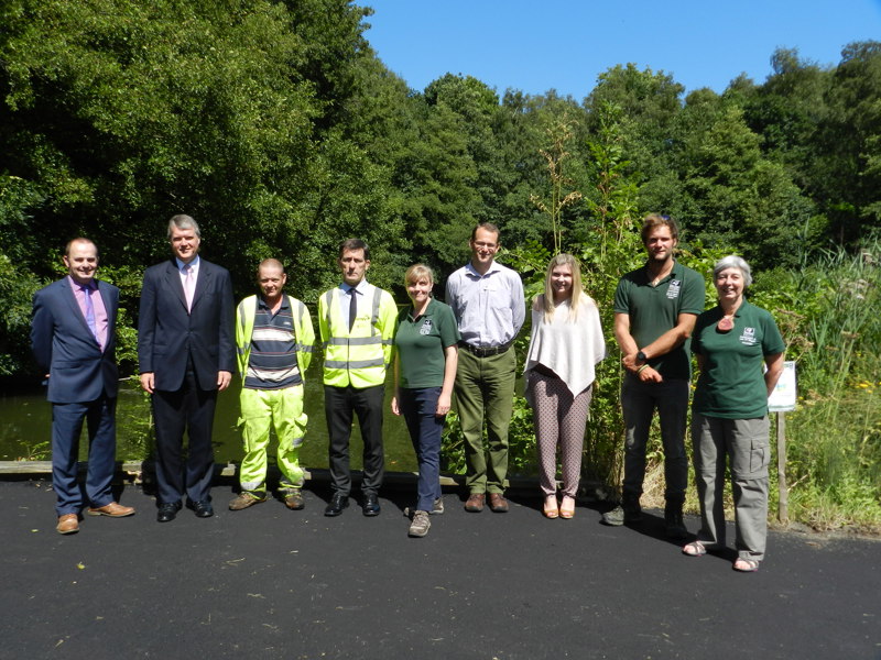 Image of people stood on a tarmacked area in front of a pond.