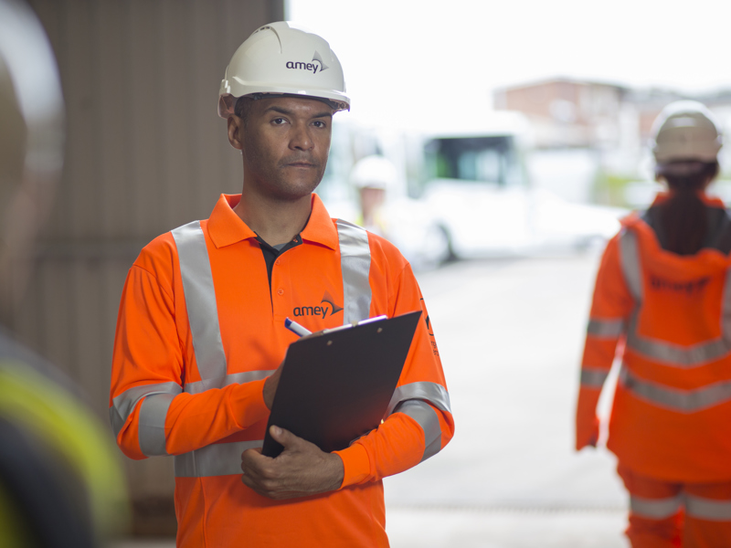 A man in PPE, holding a clipboard.