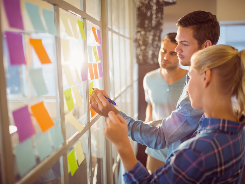 Image of men and women, placing post-it notes on a glass window.
