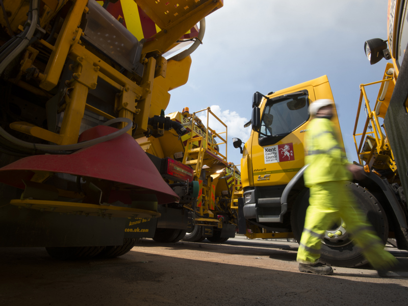 A man in PPE walking past a construction vehicle.