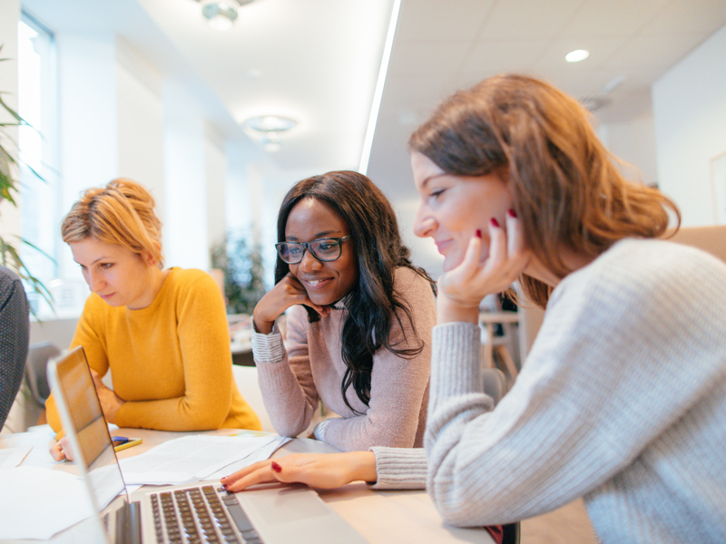 Image of three women sat at a laptop.