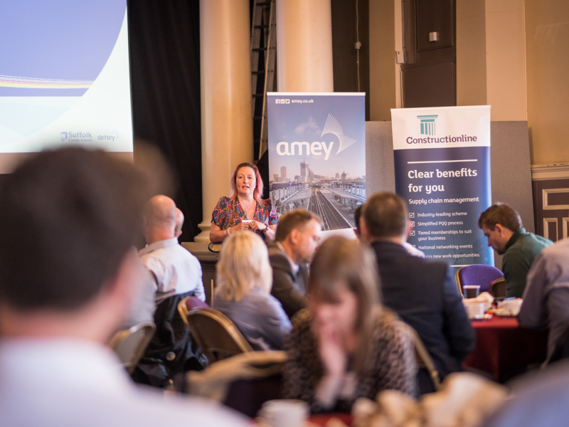Shoot of a conference. Showing people at tables, a presenter and banner stands.