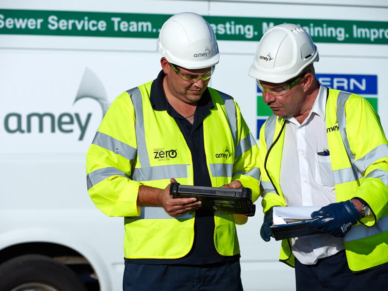 Two men in PPE, inspecting a meter reader.