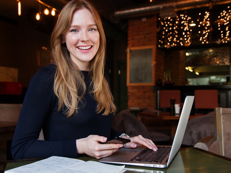 A woman sat at a desk with a mobile phone and laptop.