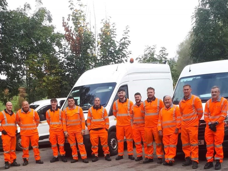 Image of a line up of Amey employees in PPE, stood in front on vans.