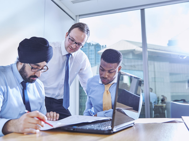 three men working at a laptop.