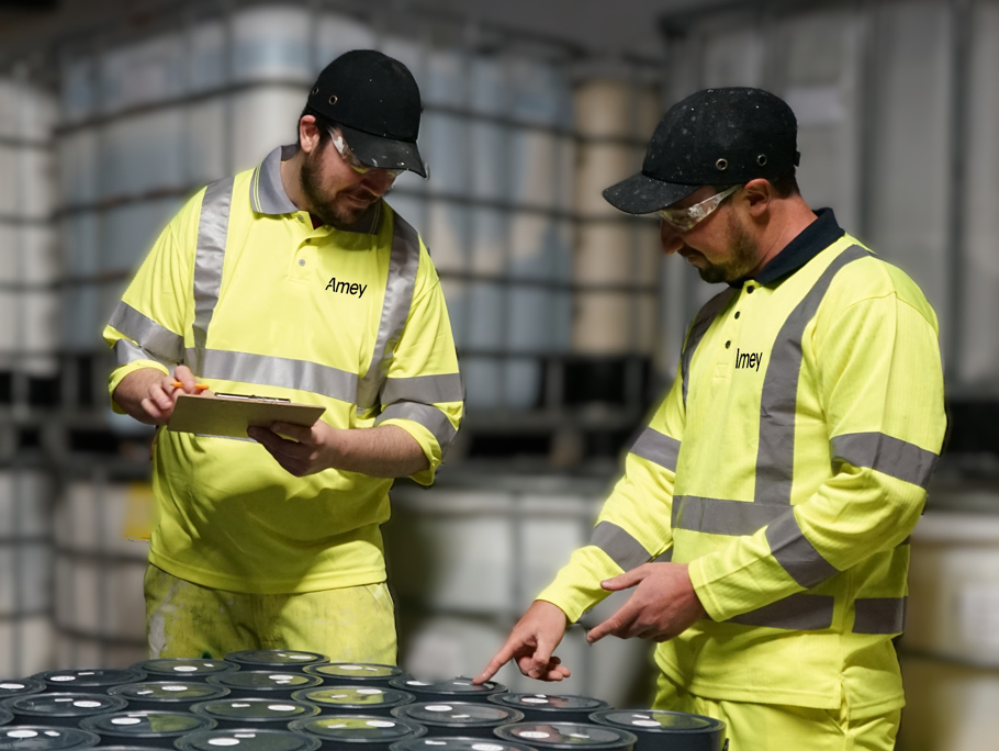 Two men in yellow PPE inspecting paint cans.