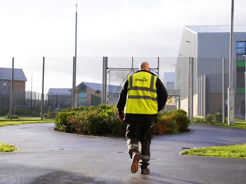 Image of an Amey employees, wearing PPE, approaching a fenced off building.